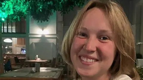 Suffolk Police A smiling Georgia looks directly at the camera, she is seated in an empty restaurant. She has short brown hair. 