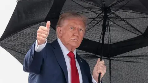 Reuters Donald Trump gives a thumbs up as he holds an umbrella before boarding Air Force One
