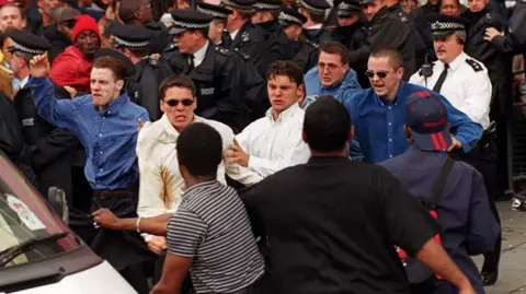PA Media Five men flanked by police officers holding back an angry crowd leave the Stephen Lawrence inquiry in 1998
