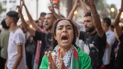 Anadolu via Getty Images A protester looks at the camera as she chants a slogan. She is wearing a green top and is clapping her hands