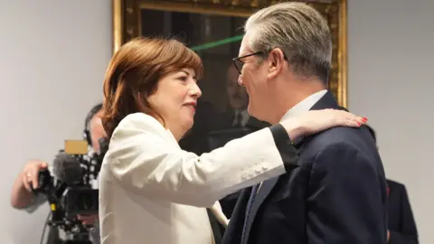 PA Media Lucy Powell, new deputy Labour leader, embracing Prime Minister Sir Keir Starmer indoors. Lucy Powell is wearing a light-colored blazer, and Sir Keir Starmer is dressed in a dark suit.