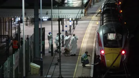 PA Media A train with people wearing forensic white suits at the station 