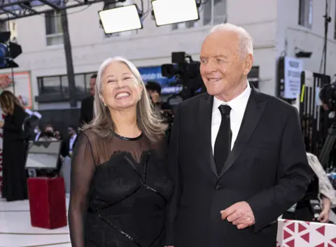 Reuters Stella on the left smiling in black chiffon and lace dress and Sir Anthony in black suit with white shirt