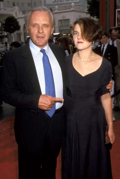 Getty Images Hopkins in black suit, white shirt and blue tie, with his arm around his daughter Abigail, short bob,  in black dress and gold necklace. Hopkins is pointing to her