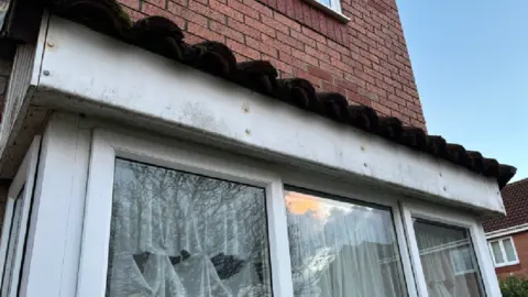An image of the outside of David's home. Mould and damp on top of the windows on the outside extension can be seen. 