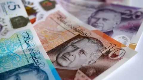 PA Media Three banknotes lying on a table - a £5, £10 and £20 overlap each other