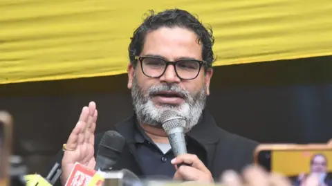 Getty Images Prashant Kishor, in a black t-shirt with a mic in his hand as he talks to reporters against a black and yellow background
