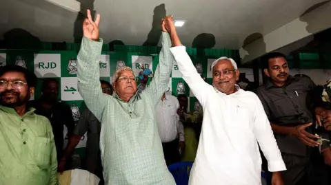 Getty Images Lalu Prasad Yadav seen in a green kurta holding up his hand with that Nitish Kumar seen in a white kurta at the RJD office in Patna on 8 November 2015