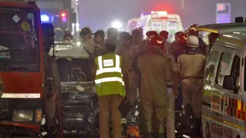 REUTERS/Stringer Fire service and other emergency personnel stand next to the exploded car, with ambulances with their lights flashing can be seen in the background