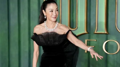 PA Media Michelle Yeoh dressed in black is pictured against a green background arriving for the European premiere of Wicked: For Good, at Cineworld Leicester Square in London. 