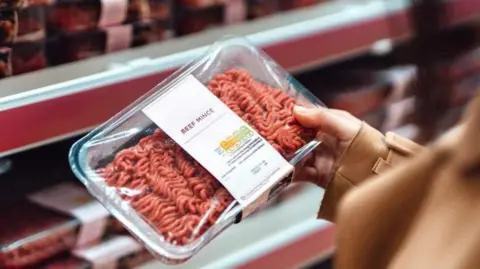 Getty Images A shopper holds a packet of beef mince in her hand in front of a supermarket shelf.