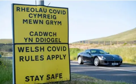 Getty Images A sign for Welsh Covid rules on the side of the road with a car driving past. 