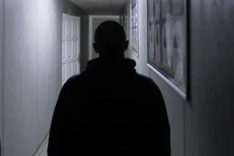 SBU A rear view of the top half of Vlad in silhouette in a poorly-lit corridor of the Rivne detention centre. His head is shaven.