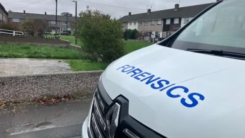 A forensics van parked at Baydon Close. The home, which has police tape outside, can be seen in the background, as well as terraced residential properties.