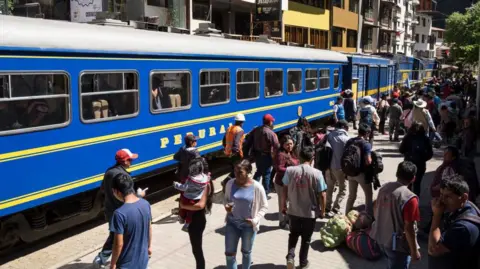AFP via Getty Images A train at the station in Aguas Calientes, with people standing on the platform