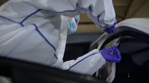 A person in a white suit is seen cutting an air bag out of a white car