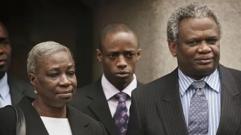 Getty Images Gloria, Tunde and Richard Taylor outside the Old Bailey in April 2006. All three wear dark coloured suits.