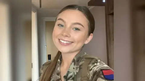 Family handout A young woman called Jaysley Beck wearing army camouflage is smiling in a selfie style photo. She has her hair pulled back into a ponytail, which is sat over her shoulder. There is a red and blue patch on the top of her sleeve.
