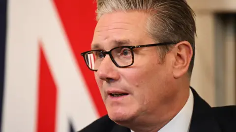 PA Prime Minister Sir Keir Starmer wears black glasses and a dark suit.