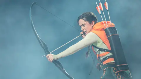 Johan Persson Mia Carragher as Katniss holding a bow and arrow 