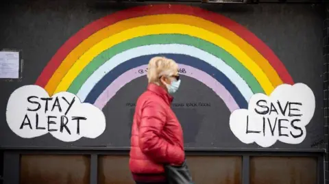 Getty Images Woman walking down street past Covid sign