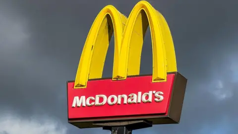 Getty Images A large McDonald's sign with the yellow arches stands in front of a gloomy grey sky.