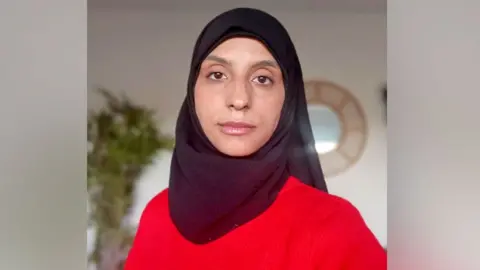 Kawtar Boudad Dupont A woman in a red jumper. She has brown eyes and is wearing a black hijab covering her hair. 