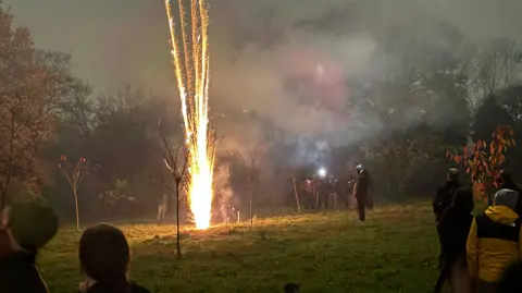 BBC Firework being set off in a Glasgow park with people gathered round.