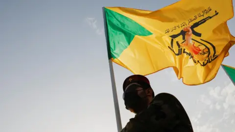 Reuters File photo showing a mourner carrying a Kataib Hezbollah flag during a funeral in Baghdad, Iraq, for a commander of the Iraqi militia who was killed in an Israeli strike in Syria (22 September 2024)