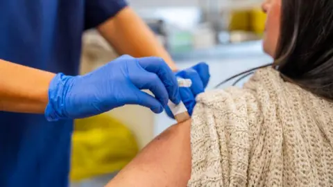 Getty Images Medical professional wearing blue gloves covering injection site with a plaster.