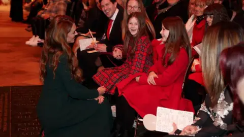Reuters Catherine crouches and smiles as she speaks to two young girls sat on chairs waiting for the service the begin 