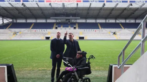 Getty Images Prince William being shown around Headingley Stadium by Kevin Sinfield. Rob Burrow is next to the pair in an electric wheelchair.