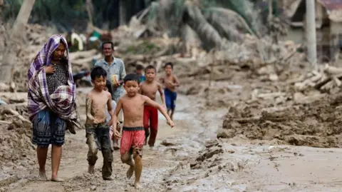 Reuters A group of people walk along a muddy road which has been left destroyed by flooding