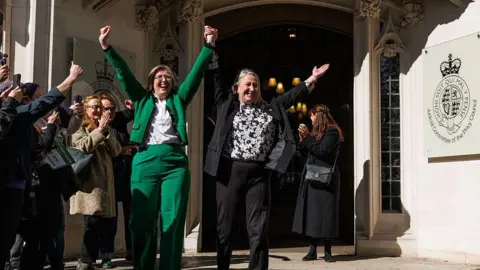 Getty Images An image of For Women Scotland campaigners Susan Smith - wearing a green suit and white shirt - and Marion Calder, wearing a black suit and black and white top - celebrating their win over the Scottish government outside the Supreme Court in London