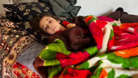 Little girl looking at the camera, lying under blankets and bedding