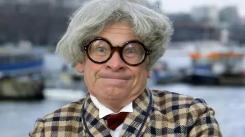 Getty Images Baxter as Mr Majeika.  He is wearing a checked suit and huge glasses and is looking into camera.