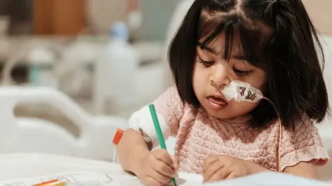 PA Media Zarwa is seen with a feeding tube concentrating on colouring a picture at a hospital table.