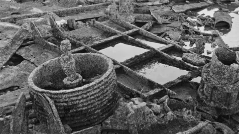 Peter Britton A black and white photo shows parts of shipwrecks on the rock