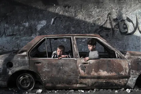 AFP via Getty Images Children sit in a destroyed car in Rafah, on the southern Gaza Strip on February 28, 2024