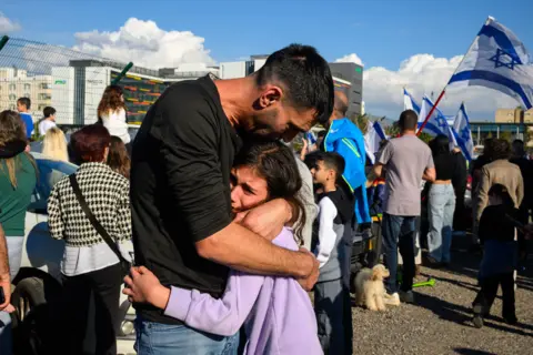 Getty Images A father comforts his daughter after the first helicopter arrived carrying hostages to Bellinson Hospital in Israel
