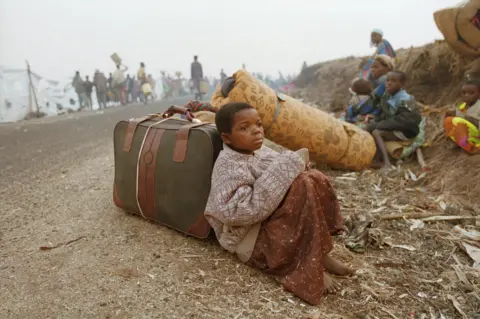 VCG via Getty Images A Rwandan girl sitting on a roadside with some luggage 