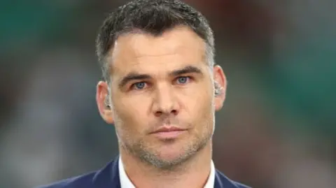 Getty Images Mike Phillips facing audience at Rugby World Cup 2019. White shirt, blue blazer, looking serious