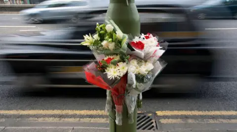 Getty Images A bouquet of flowers attached to a lamppost next to a busy road