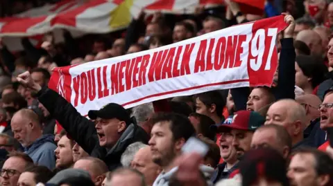 Reuters A crowd of Liverpool Football Club supporters holding a banner which reads 'You'll Never Walk Alone 97' 