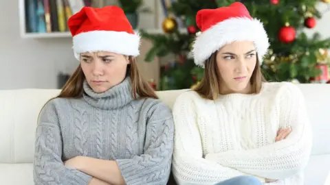 Getty Images Two sisters with their arms folded, looking cross, at Christmas while wearing father Christmas hats