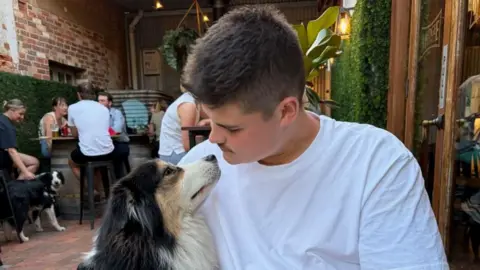 PA Media Constable Jack Hibbert dressed in a whiteT-shirt looking down at a dog and sitting in a restaurant.