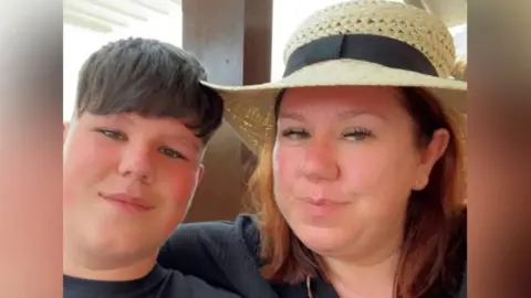 Family photo Morgan and Victoria Hopkins pictured sitting close together. Morgan wears a black t-shirt and has short brown hair and Victoria wears a black top with a v-neck and has red bobbed hair under a straw hat