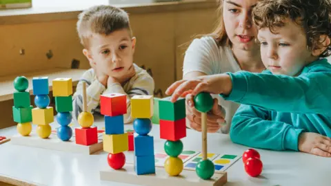Getty Images Two children and a woman are playing with colourful toys. 