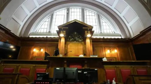 PA Media The inside of a court room. The court has red cushioned seats and wide semi-circle window. A crest is on the wall at the back of the court.