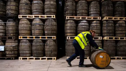 AFP via Getty Images Stacked whisky casks and a man in a high vis jack rolling a cask in the foreground